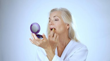 Olgun bir kadın gülümsüyor ve bir fırçayla makyaj yapıyor, parlak ve rahatlatıcı bir spa ortamında mutluluk yayıyor. Rahatlamış ve memnun görünüyor..