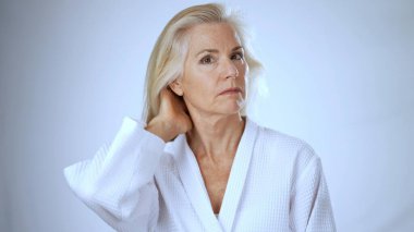 Beyaz cüppeli olgun bir kadın rahatlatıcı bir spa tedavisi sırasında saçını tararken gülümsüyor. Huzurlu arka plan, refahın rahatlatıcı atmosferine katkı sağlar..