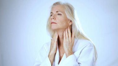 Uzun, açık renkli saçları olan olgun bir kadın spa tedavisinin keyfini çıkarırken mutlu bir şekilde gülümser. Beyaz arka planda huzurlu bir atmosfer sunar..