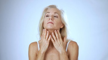 Parlak bir kaplıcada olgun bir kadın cilt bakım ürünleri uygularken neşeyle gülümsüyor. Sakin atmosfer onun rahatlığını ve güzellik deneyimini arttırıyor..