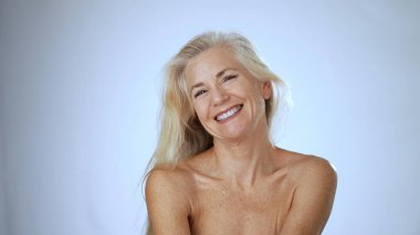 Uzun saçlı olgun bir kadın mutlu bir şekilde gülümsüyor, huzurlu, aydınlık bir atmosferde bir spa 'da rahatlama anını kucaklıyor..