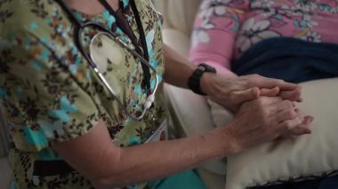 İlgili bir hemşire sıcak bir bakım ortamında yaşlı bir kadının elini nazikçe tutar. Onların bağlantıları ziyaret sırasında sıcaklığı ve merhameti yansıtır..