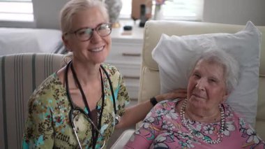 Gülümseyen hemşire, huzur ve bakım tesisinde yaşlı bir kadının hayati organlarını kontrol ederken dostça bir sohbete girişir..