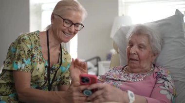 Şefkatli bir hemşire yaşlı bir kadınla, yaşlılar yurduna yaptığı ziyarette akıllı telefondan fotoğraf ve anılarını paylaşarak yakınlaşır..