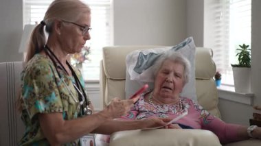 Hemşire ve yaşlı bir kadın, huzur evinde hayati organlarını kontrol ederken dostça bir konuşma yaparak bakım için destekleyici bir ortam yaratıyorlar..