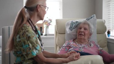 Bir hemşire yaşlı bir kadının elini tutarken onu huzur evinde dostça bir sohbete sokuyor. İkisi de mutlu ve nişanlı görünüyor..