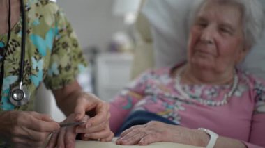 Bir hemşire, yaşlı bir kadının tırnaklarını nazikçe ilgi ve özen ile törpüler ve hasta için hijyen ve konfor sağlar..