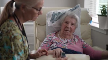 Gülümseyen bir hemşire yaşlı bir kadının oksijen seviyesini kontrol eder. Yaşlı bir yaşam tesisinde rutin bir sağlık değerlendirmesi sırasında oksimetre kullanır..