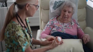 Neşeli bir hemşire, huzur ve refahını sağlamak için huzurevinde yaşlı bir kadının reçeteli ilaçlarını izlerken sohbet eder..