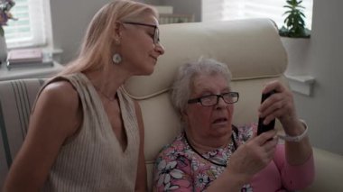 Bir kız, yaşlı annesine yaşlılar yurduna yaptığı bir ziyarette akıllı telefondan nasıl arama yapılacağını öğrenmesi için yardım ediyor..