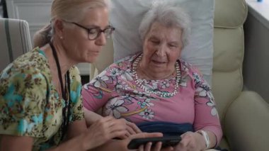 Mutlu hemşire yaşlı bir kadınla konuşuyor, sıcak ve davetkar bir ortamda huzur evini ziyaret ederken anılarını ve bilgilerini telefonla paylaşıyor..