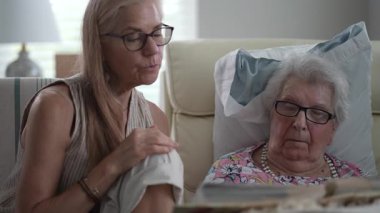 Bir kız ve yaşlı annesi, birlikte geçirdikleri özel zamanların tadını çıkardıkları bir huzurevinde fotoğraf albümünü anarken gülümsüyor ve gülüyorlar..