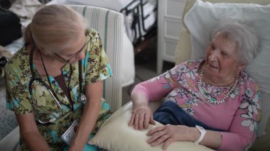 Neşeli bir hemşire yaşlı bir kadınla konuşurken huzur ve refahını sağlamak için huzurevinde yaşam belirtilerini kontrol eder..