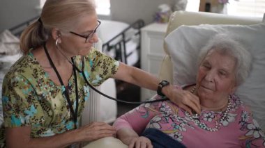 İlgili bir hemşire, yaşlı bir kadının yaşam belirtilerini kontrol ederken aynı zamanda yaşlılar için bir yaşam tesisinde arkadaşça sohbet ederek, sağlık ve arkadaşlığı teşvik eder..