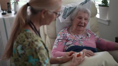 Yaşlı bir kadın, bir huzurevine sıcak bir ziyaret sırasında hayati organlarını kontrol eden bir hemşireyle mutlu bir şekilde iletişim kuruyor..