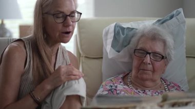 Yaşlılar yurdunda, bir kız ve yaşlı annesi birlikte gülerek hatıralarla dolu bir fotoğraf albümünü anarlar..