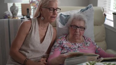 Huzurevinde, bir kız ve yaşlı annesi bir fotoğraf albümüne bakarken neşeli anılarını paylaşırken gülümsüyorlar..