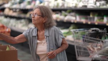 Yaşlı bir son sınıf öğrencisi, taze ürünlerle dolu bir markette alışveriş yaparken muz toplayıp poşete koyar..