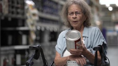 Yaşlı bir kadın, ev dekorasyon projesi için renk seçeneklerine odaklanarak bir hırdavatçıda boya kutularını karıştırıyor. Düşünceli ve seçimiyle meşgul görünüyor. Walker 'da oturuyor..