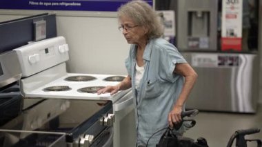 Son sınıf bir kadın, bir hırdavatçıda mutfak aletlerini karıştırmak için yürütecini kullanıyor. Ev yenileme projesi için doğru eşyaları bulmaya odaklanmış gibi görünüyor..