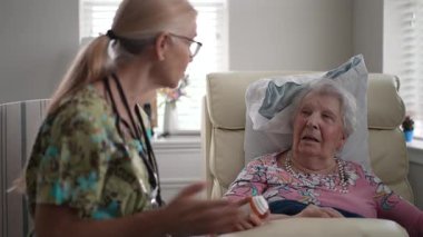 Huzurevindeki yaşlı bir kadını ziyaret eden bir hemşire, sağlık ve günlük hayatı hakkında keyifli bir konuşma yaparken hayati organlarını kontrol ediyor..