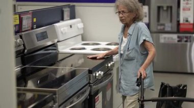 Yürüteçli yaşlı bir kadın, bir hırdavatçıda çeşitli ev dekorasyonu aletlerini karıştırıyor ve yeni projelerine odaklanıyor..