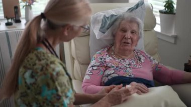 Bir hemşire, rutin bir ziyaret sırasında hayati organlarını kontrol ederken gülümseyen mutlu ve yaşlı bir kadınla hoş bir sohbet eder..