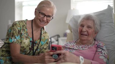 Yaşlı bir kadınla oturma odasında anılarını ve bilgilerini paylaşırken hemşirenin portresi, ziyaret deneyimlerini geliştirmek ve iletişim kurmak için akıllı telefon kullanıyor..