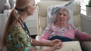 Bir hemşire, yaşlı bir kadının elini tutarak huzur evinde dostça bir konuşma yaparak sıcak bir destek ortamı yaratıyor..