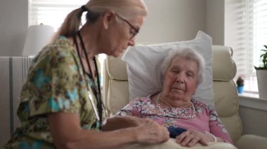 Hemşire, yaşlı bir kadının tırnaklarını rahatça törpülüyor. İlgili etkileşim, ziyaret sırasında bir anlık şefkat ve kişisel ilgiyi vurgular..