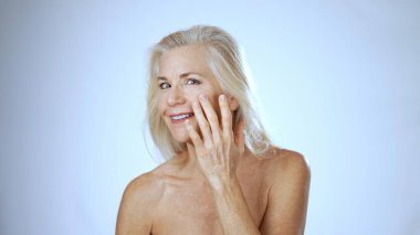 Olgun bir kadın spa ortamında rahatlar, gülümser ve cilt bakımına odaklanır. Işıltılı mutluluğu onu çevreleyen huzurlu çevreyi yansıtıyor..