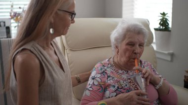 Olgun bir kadın, yaşlı annesinin pipetle su içmesini sevgiyle seyreder. Evde geçirdikleri zamanın tadını çıkarırlar..