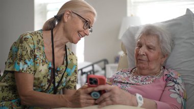 Huzurevine yapılan bir ziyarette, bir hemşire ve yaşlı bir kadın akıllı telefon kullanarak anılarını ve bilgilerini paylaştılar..