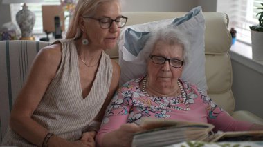 Huzurevinde, bir kız ve yaşlı annesi bir fotoğraf albümüne bakarken neşeli anılarını paylaşırken gülümsüyorlar..