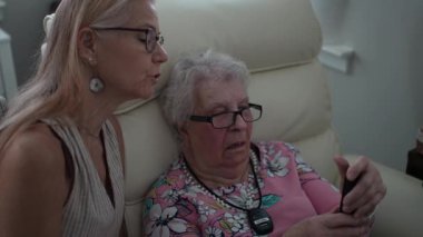 Bir kız, yaşlı annesine bir huzurevinde telefon açması için yardım eder. Hafıza becerilerini arttırmak ve tuşlamak için odaklanır..