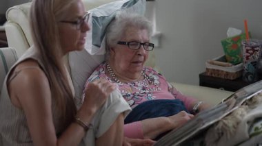 Huzurevinde, bir kız ve yaşlı annesi bir fotoğraf albümünü incelerken gülümsüyor, mutlu anılarını paylaşıyor ve kahkahalar atıyorlar..