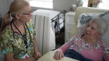 Huzurevinde, mutlu bir hemşire yaşlı bir kadının hayati organlarını kontrol ederken onunla sıcak bir konuşma yapar, iletişim kurar ve ilgilenir..