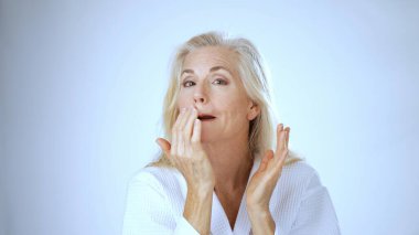 Sakin bir spa ortamında olgun bir kadın uzun saçlarını tarar, mutluluk ve sükunet saçar, parlak beyaz arka planlarla çevrilidir..