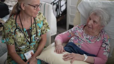 Hemşire, yaşlı bir kadınla, huzur evinin sıcak ve dostane atmosferinde hayati organlarını kontrol ederken hoş sohbetler ediyor..