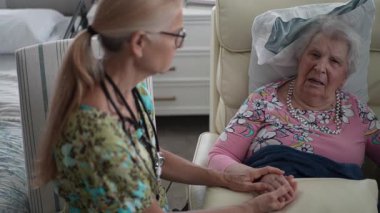 Yaşlı bir kadın, bir huzurevinde sıcak, dostane bir sohbet sırasında elini tutan bir hemşireden ilgi görüyor..