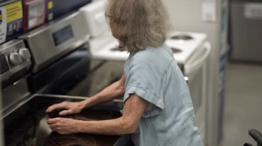 Son sınıf öğrencisi bir kadın, bir hırdavatçıdan ev dekorasyonu malzemeleri alırken yürüteç kullanıyor. Çeşitli alet ve eşyaları dikkatlice inceliyor..