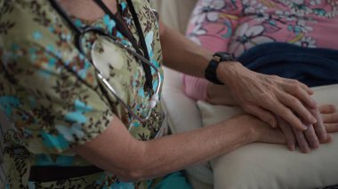 İlgili bir hemşire sıcak bir bakım ortamında yaşlı bir kadının elini nazikçe tutar. Onların bağlantıları ziyaret sırasında sıcaklığı ve merhameti yansıtır..