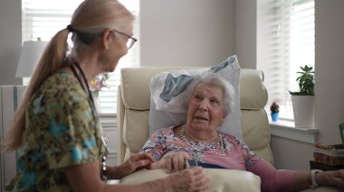 Mutlu, gülümseyen, kendini işine adamış bir hemşire yaşlı bir kadının oksijen seviyesini ölçmek için, rutin bir sağlık değerlendirmesi sırasında sağlığını sağlama almak için bir oksimetre kullanır..