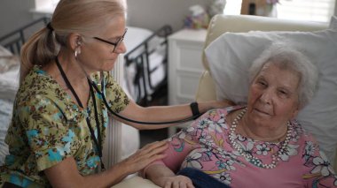 İlgili bir hemşire, yaşlı bir kadının yaşam belirtilerini kontrol ederken aynı zamanda yaşlılar için bir yaşam tesisinde arkadaşça sohbet ederek, sağlık ve arkadaşlığı teşvik eder..
