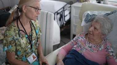 Hemşire, huzurevinde arkadaşça sohbet ederken yaşlı bir kadının hayati organlarını kontrol ediyor..