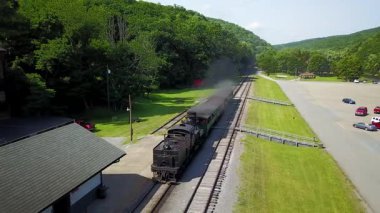 Cass Olay Yeri İnceleme trenini izleyen hava kamerası yolcularla dolu bir istasyona doğru giderken birkaç turist vagonunu geriye çekiyor..