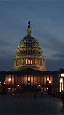 Dikey video, gece vakti Washington DC 'de gece mavisi bir gökyüzüne karşı dalgalanan ışık ve bayraklarla Kongre Binası' na akın ediyor..