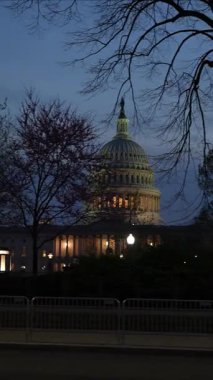 ABD Kongre Binası 'nı gece Washington DC' de mavi mor gökyüzüne karşı sallanan ışık ve bayraklarla gösteren dikey video.