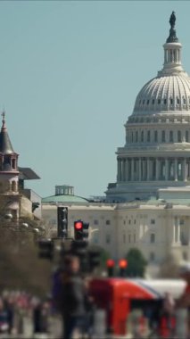 ABD Kongre Binası 'nın dikey videosu açık mavi gökyüzünün altında duruyor. Arabalar caddelerde geziniyor ve bayraklar bölgeyi süslüyor, hareketli bir atmosfer yaratıyor..