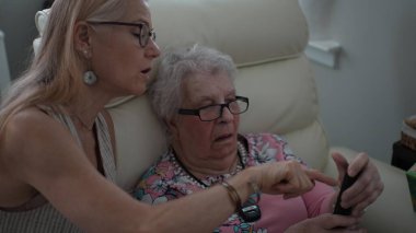 Bir kız, yaşlı annesine bir huzurevinde telefon açması için yardım eder. Hafıza becerilerini arttırmak ve tuşlamak için odaklanır..